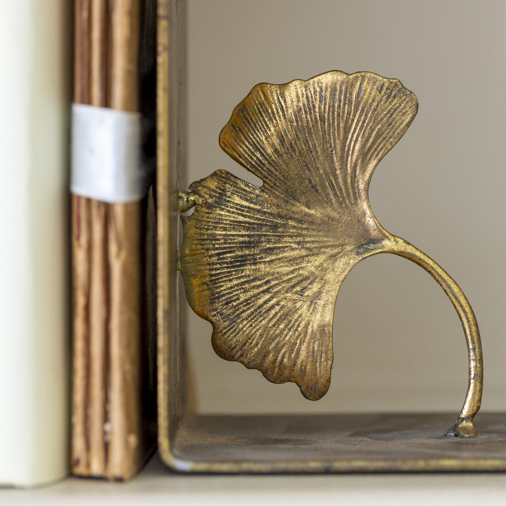 Detail of right hand lotus leaf gold bookend propping up books on a shelf for elevated, timeless shelf styling